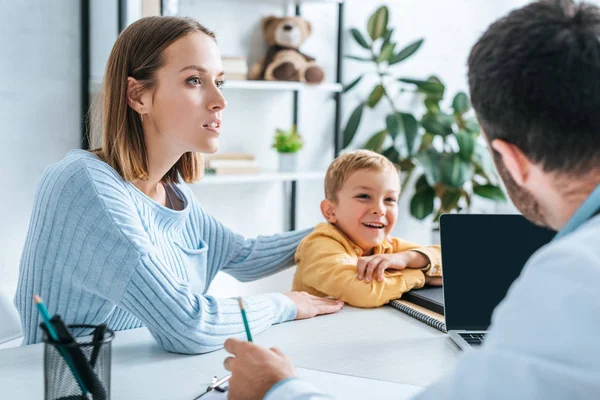 Mère attentive et fils souriant regardant le médecin à l'hôpital — Photo de stock