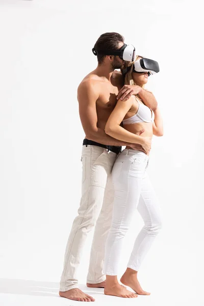 Beautiful passionate couple in Vr headsets hugging on white — Stock Photo