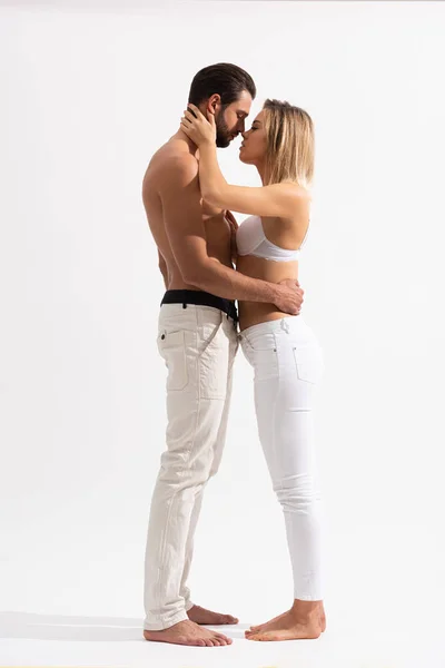 Vista lateral de hermosa pareja seductora abrazándose e ir a besarse en blanco - foto de stock