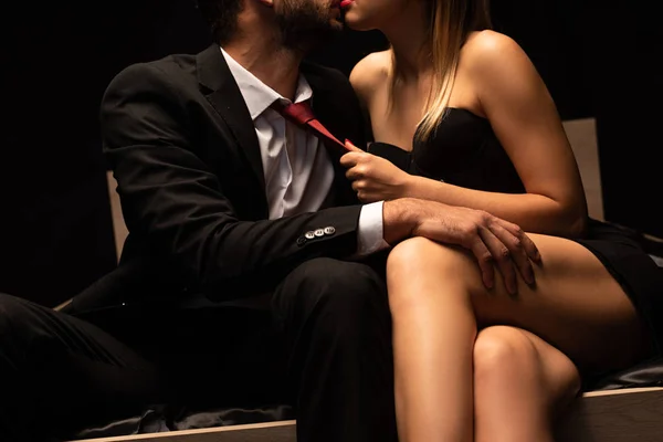 Обрізаний вид сексуальної жінки тримає краватку чоловіка в ліжку в темній кімнаті — стокове фото