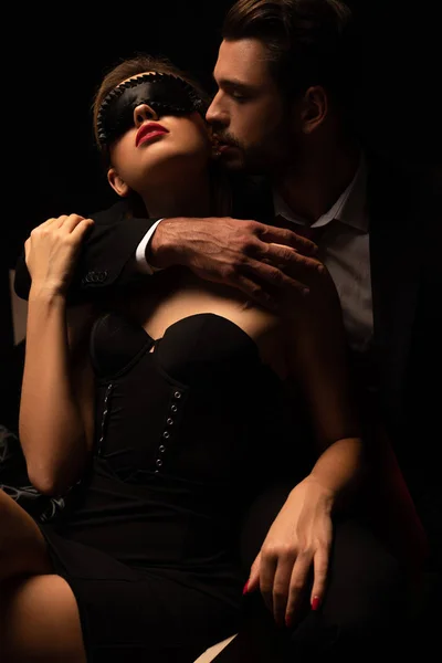 Leidenschaftlicher Mann umarmt Frau in Maske auf Bett in dunklem Raum — Stockfoto