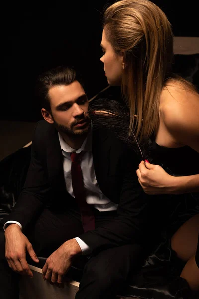 Apasionada joven pareja de amantes jugando con pluma en la cama en habitación oscura — Stock Photo