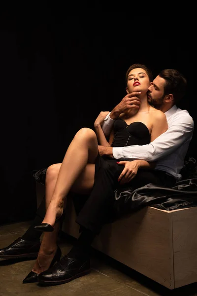 Beau couple passionné d'amoureux assis sur le lit dans la chambre noire — Photo de stock