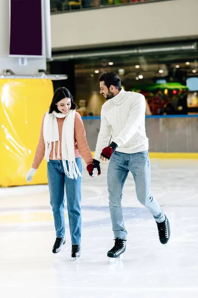 Alegre joven pareja cogido de la mano y patinaje sobre pista de patinaje - foto de stock