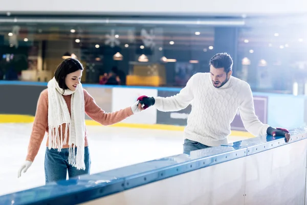 Fröhliche junge Frau bringt Mann beim Händchenhalten das Skaten auf einer Eisbahn bei — Stockfoto