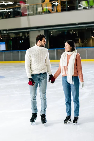 Belo casal sorrindo de mãos dadas na pista de patinação — Fotografia de Stock