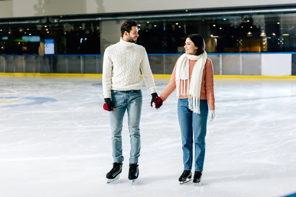 Hermosa feliz pareja cogida de la mano en pista de patinaje - foto de stock