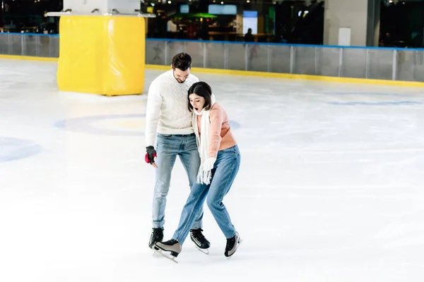 Junges Paar skatet zusammen, während Frau auf Eisbahn stürzt — Stockfoto