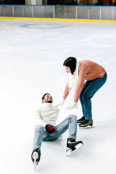 Jeune couple positif patinant ensemble pendant que l'homme tombe sur la patinoire — Photo de stock
