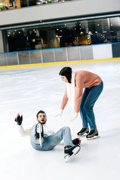 Worried couple spending time on skating rink while man falling on rink — Stock Photo
