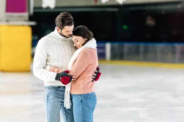 Jeune couple en chandails étreignant sur la patinoire — Photo de stock