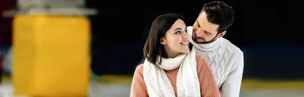 Plano panorámico de joven sonriente pareja en suéteres abrazándose en pista de patinaje - foto de stock