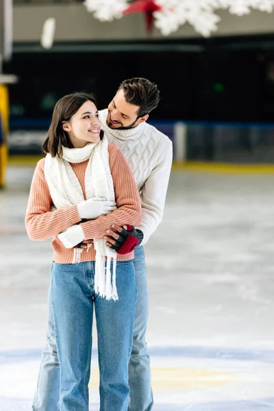 Felice giovane coppia in maglioni che si abbraccia sulla pista di pattinaggio — Foto stock