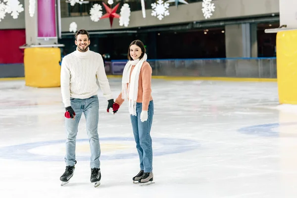 Sorridente giovane coppia che si tiene per mano sulla pista di pattinaggio — Foto stock