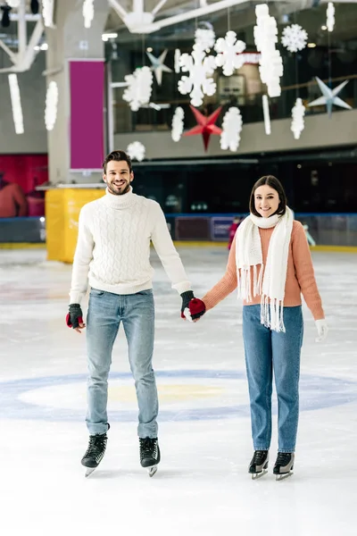 Lächelndes junges Paar hält Händchen beim Schlittschuhlaufen auf der Eisbahn — Stockfoto