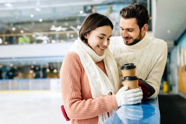 Belo casal feliz segurando café para ir na pista de patinação — Fotografia de Stock