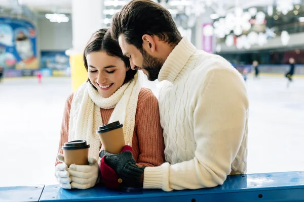 Beautiful happy couple smiling and holding coffee to go on skating rink — Stock Photo