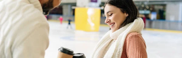 Plano panorámico de alegre pareja joven sosteniendo café para ir en pista de patinaje - foto de stock