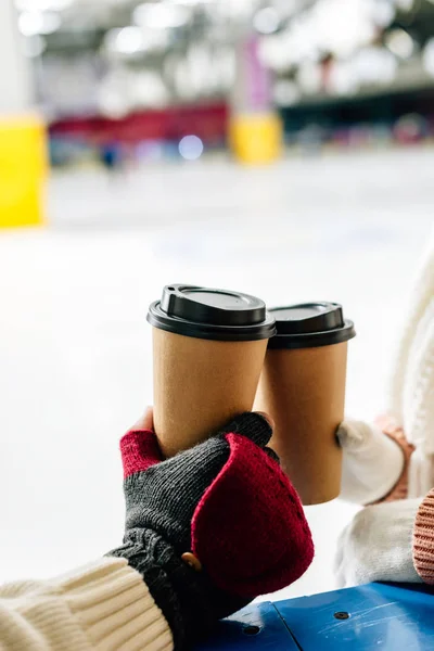 Vista recortada de la pareja sosteniendo tazas de café desechables para ir en pista de patinaje - foto de stock
