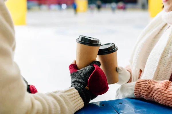 Cropped view of couple holding paper cups of coffee to go on skating rink — Stock Photo