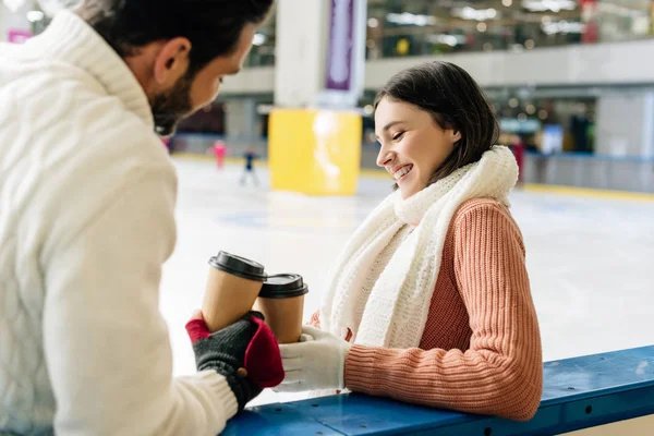 Beautiful girlfriend and happy boyfriend holding coffee to go on skating rink — Stock Photo
