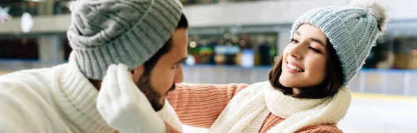 Panoramic shot of young happy couple wearing hats on skating rink — Stock Photo
