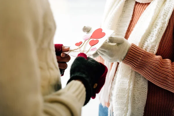 Cropped view of man giving greeting card with hearts on valentines day to woman on skating rink — Stock Photo