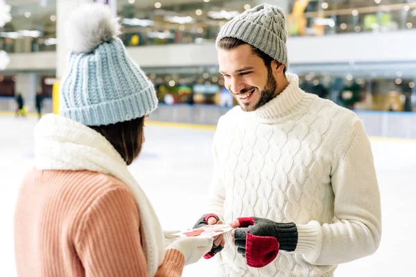 Homme souriant donnant carte de voeux sur la Saint-Valentin à la femme sur la patinoire — Photo de stock