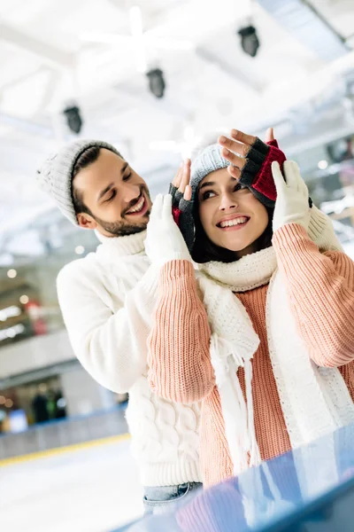 Sonriente hombre cerrando los ojos a feliz chica para hacer una sorpresa en pista de patinaje - foto de stock