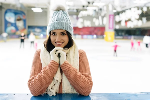Lächelndes Mädchen in Pullover, Schal, Handschuhen und Mütze auf der Eisbahn — Stockfoto