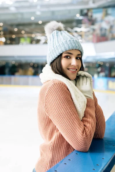 Beautiful smiling girl in sweater, scarf, gloves and hat standing on skating rink — Stock Photo