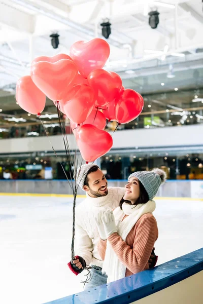 Красива пара з повітряними кулями у формі червоного серця проводить час на ковзанах в день валентинки — стокове фото