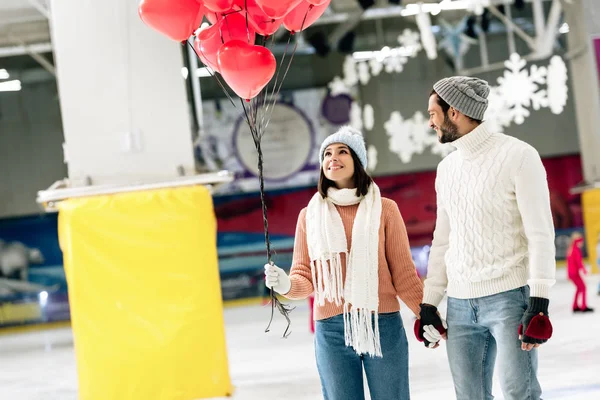 Coppia allegra con palloncini a forma di cuore rosso trascorrere del tempo sulla pista di pattinaggio il giorno di San Valentino — Foto stock