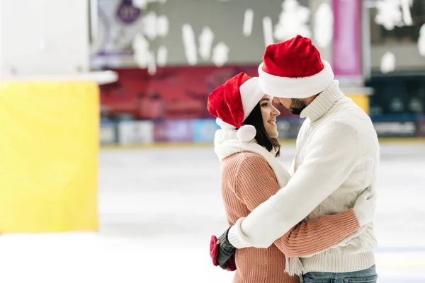 Beautiful couple in santa hats spending time on skating rink — Stock Photo