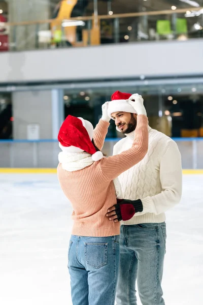 Beautiful happy couple in santa hats spending time on skating rink — Stock Photo