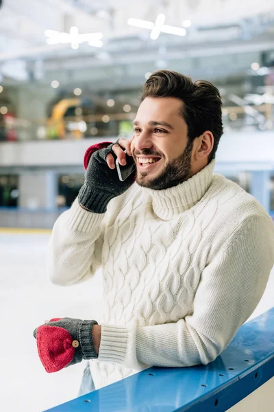 Ein fröhlicher Mann im Pullover spricht auf der Eisbahn mit dem Smartphone — Stockfoto
