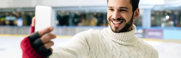 Panoramic shot of happy man taking selfie on smartphone on skating rink — Stock Photo