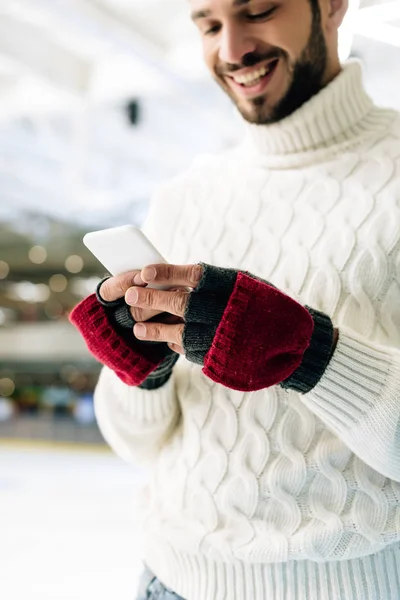 Hombre alegre en suéter usando smartphone en pista de patinaje - foto de stock