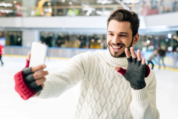 Cheerful man waving hand and using smartphone on skating rink — Stock Photo