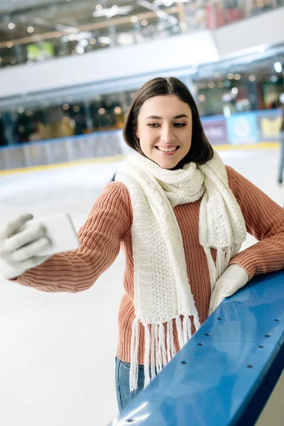 Bela menina sorridente tomando selfie no smartphone na pista de patinação — Fotografia de Stock