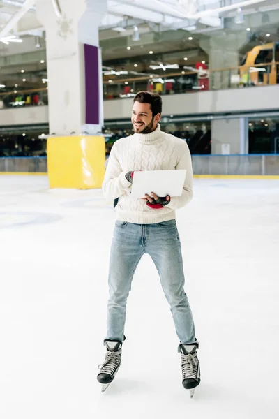 Cheerful man standing on skating rink with laptop — Stock Photo