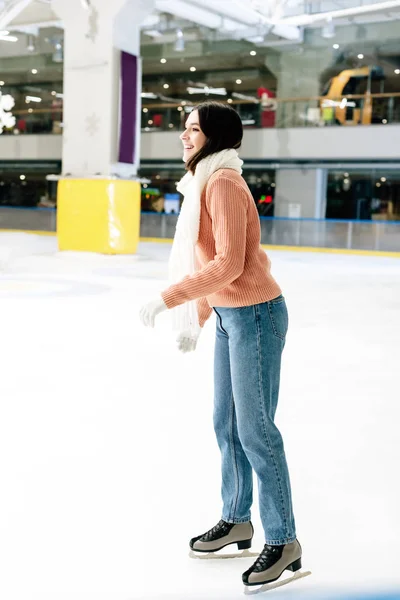 Cheerful girl in sweater and scarf skating on rink — Stock Photo