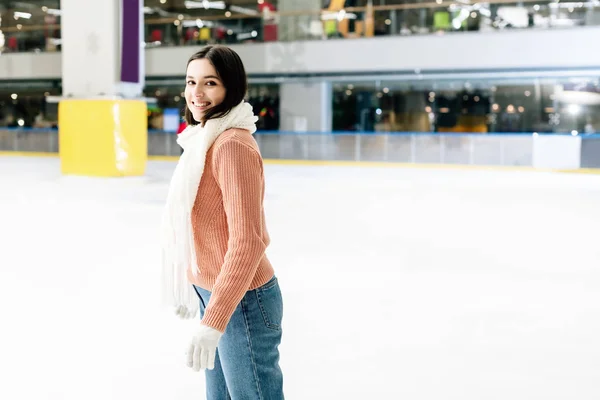 Hermosa chica feliz en suéter y bufanda patinaje en pista de patinaje - foto de stock