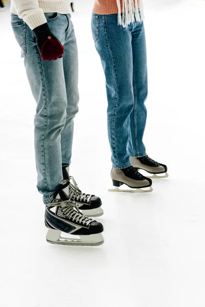 Vista recortada de pareja joven en jeans y patines de pie en pista de patinaje - foto de stock