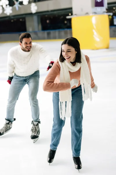 Joven pareja positiva divertirse mientras patina en pista de patinaje - foto de stock