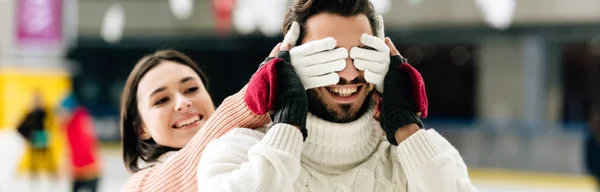 Colpo panoramico di bella donna che chiude gli occhi all'uomo sorridente per fare una sorpresa sulla pista di pattinaggio — Foto stock