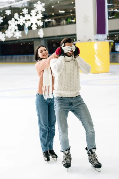 Cheerful woman closing eyes to man to make a surprise on skating rink — Stock Photo