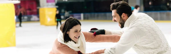 Plan panoramique de joyeux jeune couple s'amusant sur la patinoire — Photo de stock