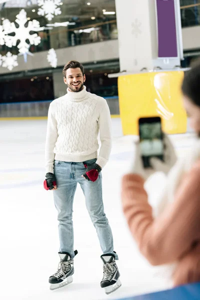 Selective focus of woman taking photo of handsome smiling man on smartphone on skating rink — Stock Photo