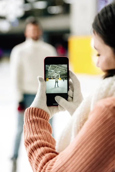 Селективный фокус женщины, фотографирующей мужчину на смартфоне на катке — стоковое фото